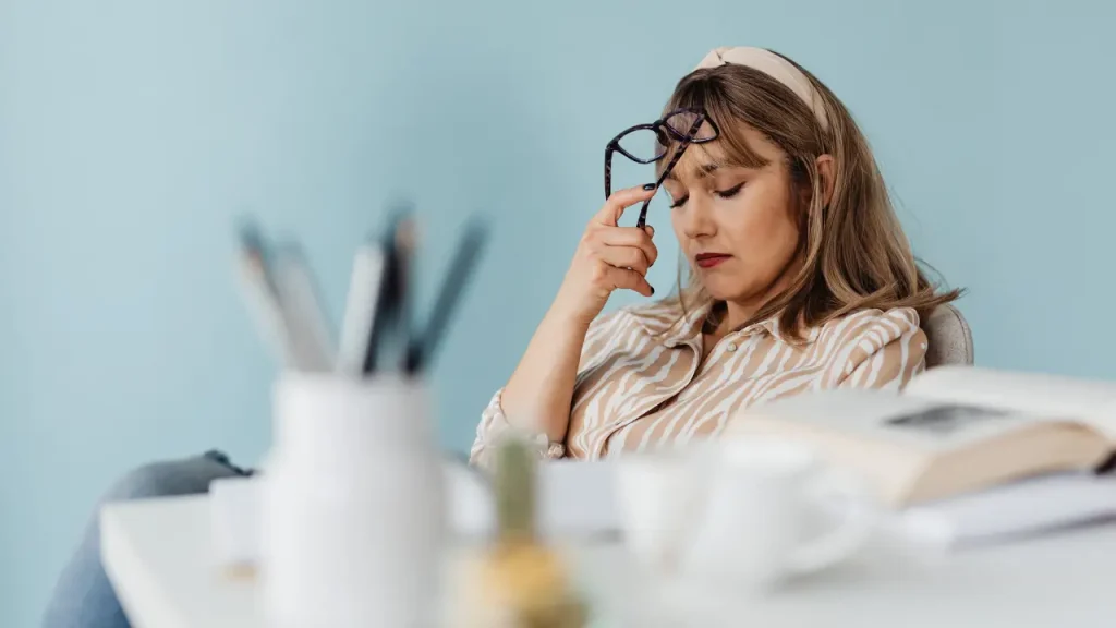 Mulher segurando óculos visivelmente abatida mostrando o que é síndrome de burnout

